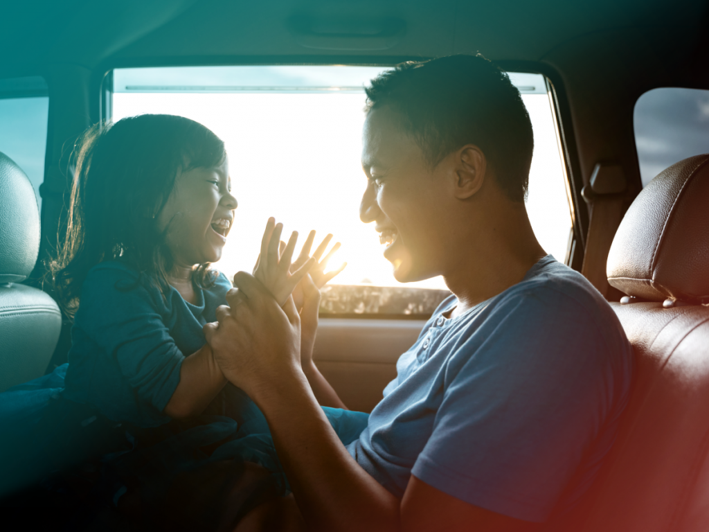 Father and daughter playing and laughing together in a car.