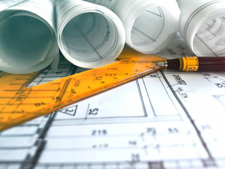 Architecture blueprints next to a ruler and a pen.