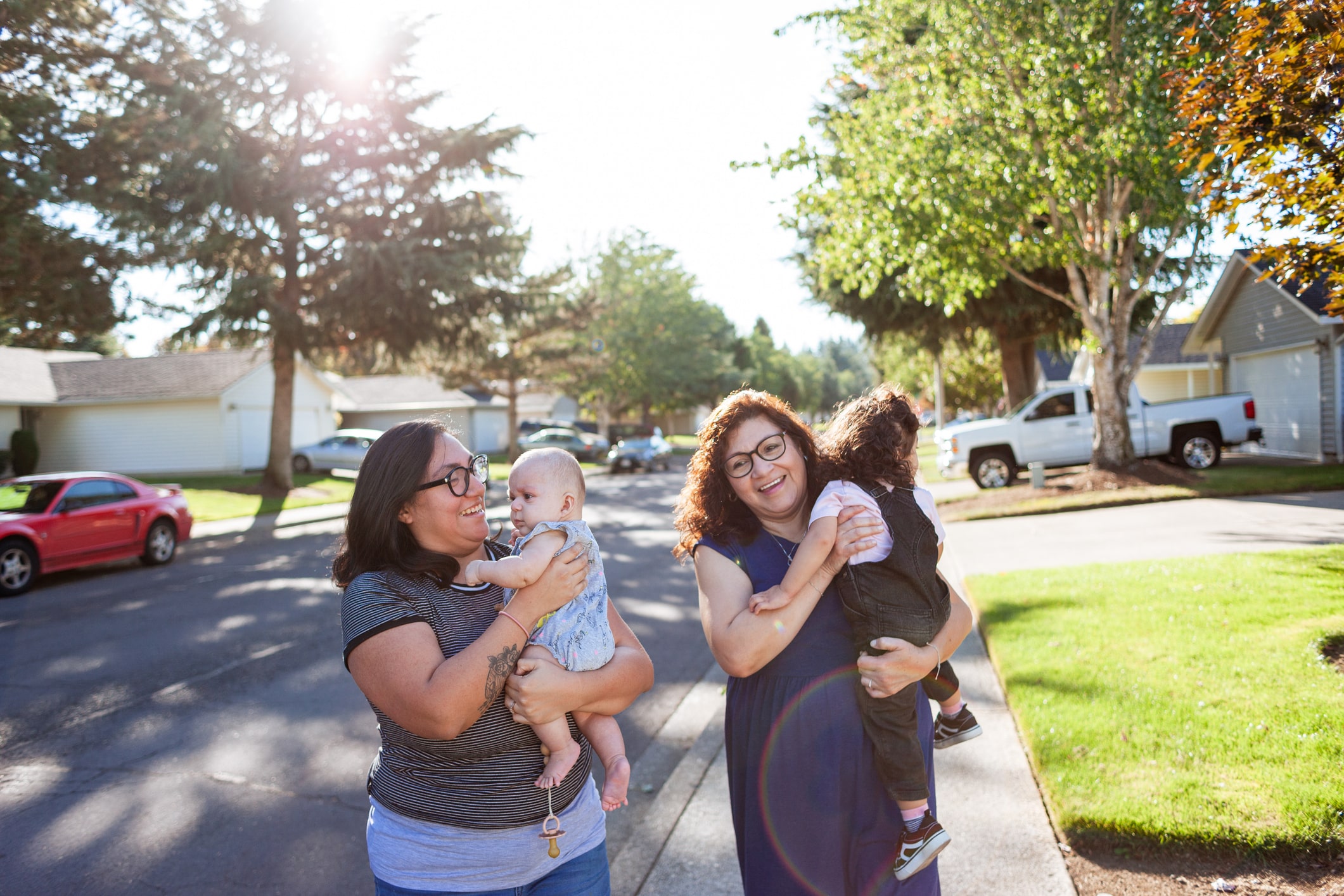 A multigenerational family of Latina women walking through a neighborhood, grandma, mother and two baby daughters. Shot in end of summer, September.